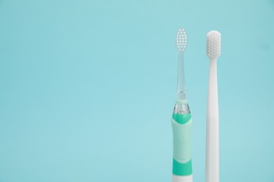 Photo of Electric and plastic toothbrushes on light blue background, space for text