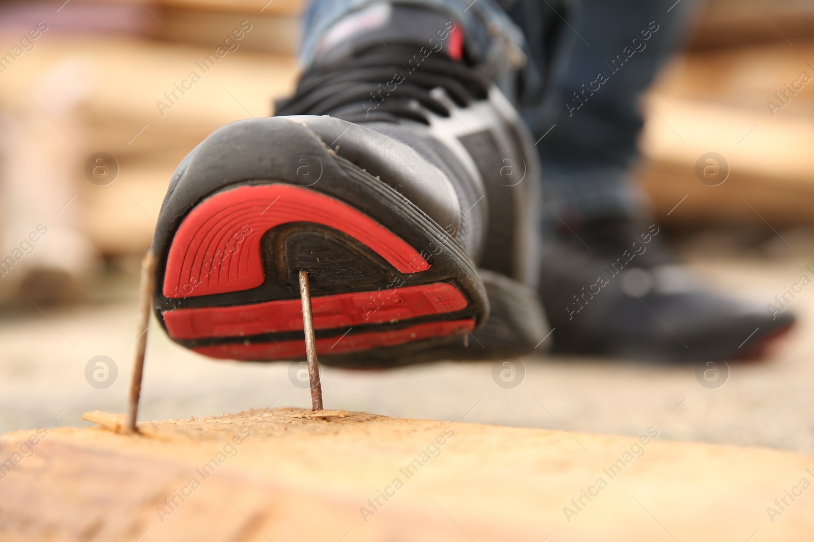 Photo of Careless worker stepping on nails in wooden plank outdoors, closeup