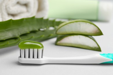 Toothbrush with toothpaste and fresh aloe on light grey background, closeup