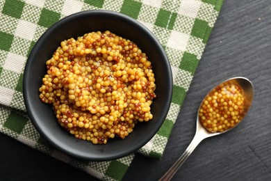 Photo of Bowl and spoon with whole grain mustard on black wooden table, flat lay