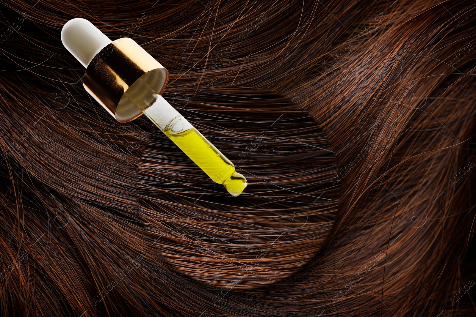 Image of Dripping cosmetic oil from pipette onto brown hair in zoomed area