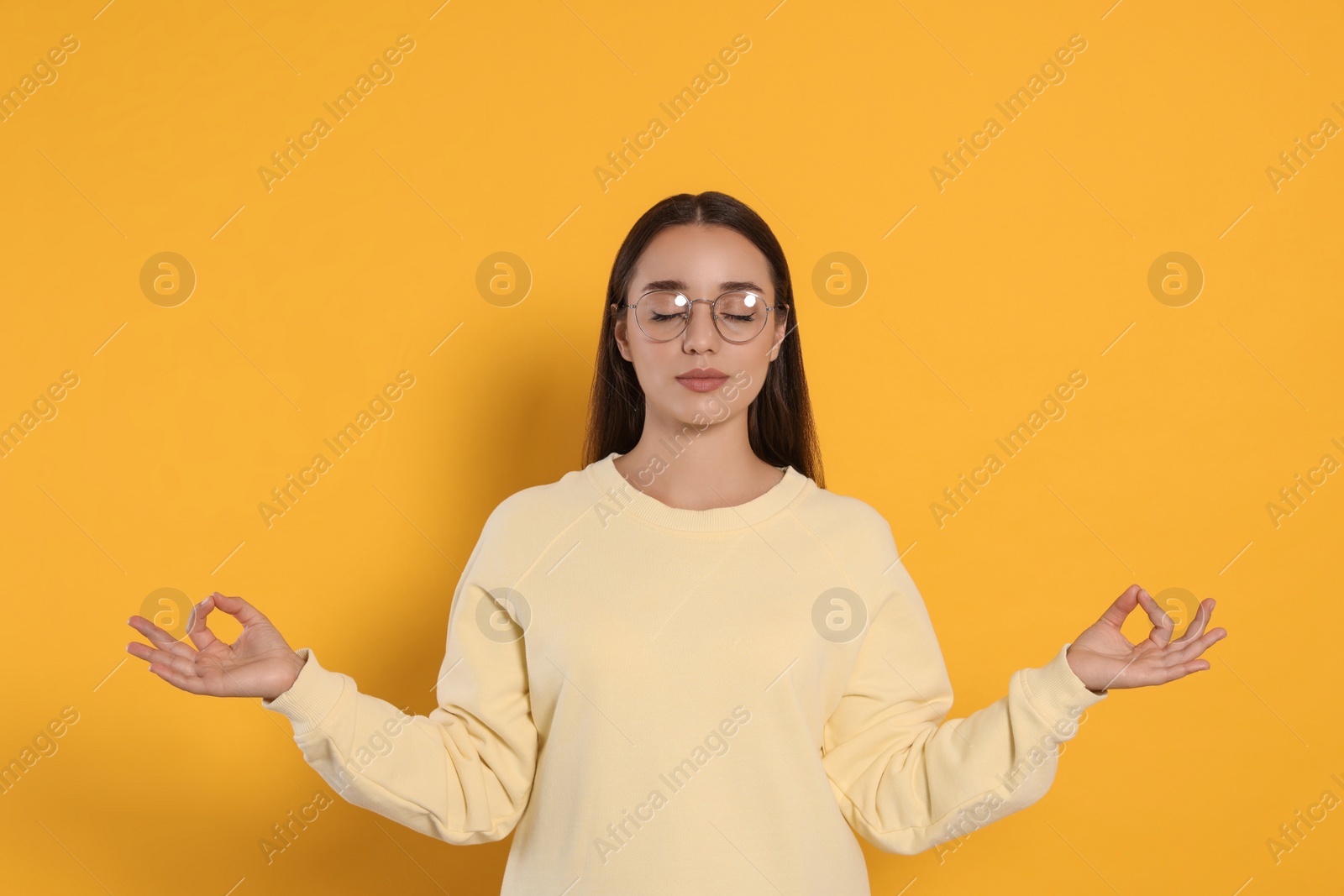 Photo of Find zen. Beautiful young woman meditating on yellow background