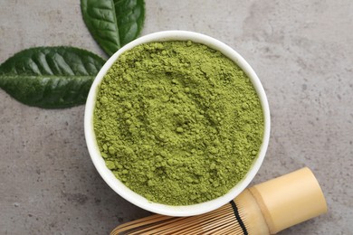 Photo of Green matcha powder, bamboo whisk and leaves on light grey table, flat lay