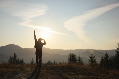 Photo of Silhouette of woman at sunrise in mountains, back view. Space for text