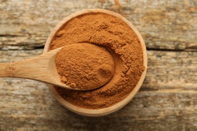 Taking cinnamon powder with spoon from bowl on wooden table, top view