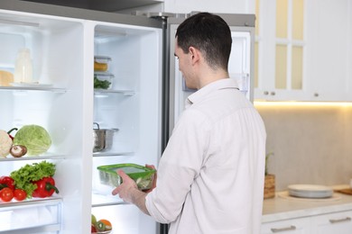 Photo of Man putting container with vegetables into refrigerator in kitchen