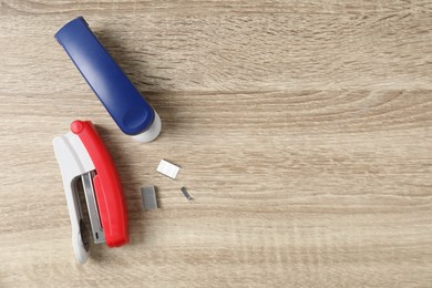 Color staplers and metal staples on wooden table, flat lay. Space for text