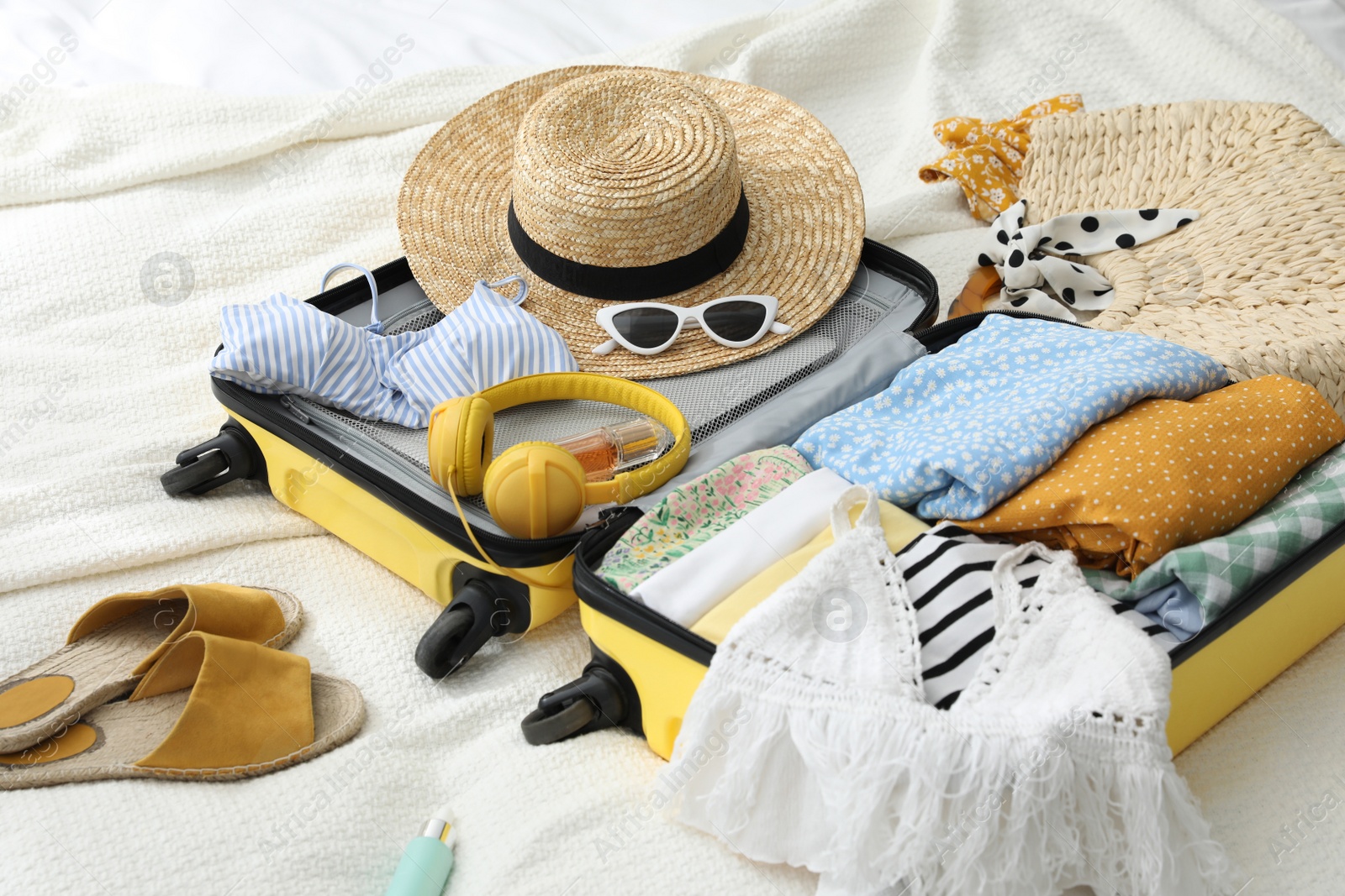 Photo of Open suitcase full of clothes, shoes and summer accessories on bed