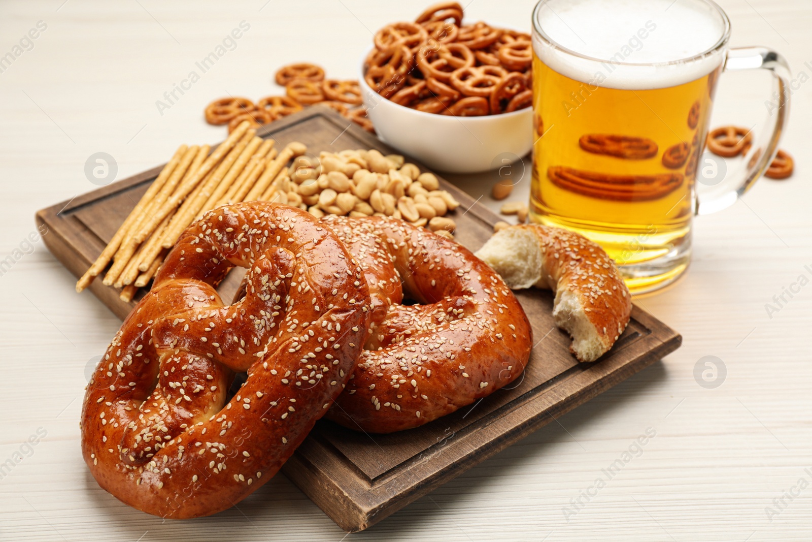 Photo of Glass of beer served with delicious pretzel crackers and other snacks on white wooden table