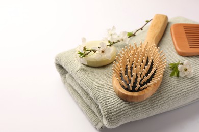 Photo of Wooden hairbrush, solid shampoo, comb, towel and branches with flowers on white background. Space for text, closeup.