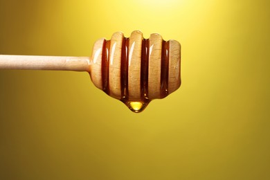 Photo of Delicious honey flowing down from dipper against golden background, closeup. Space for text