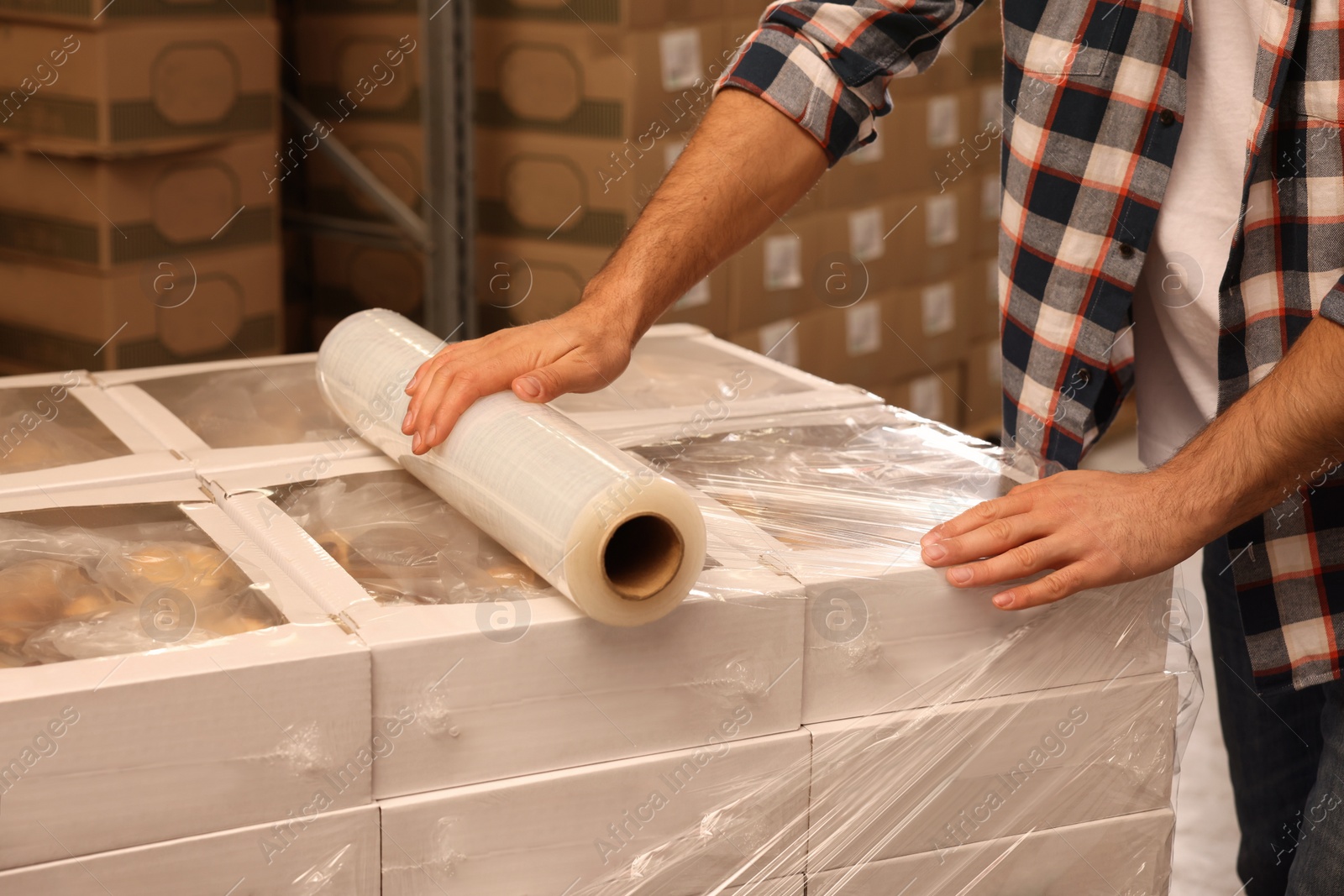 Photo of Worker wrapping boxes in stretch film at warehouse, closeup