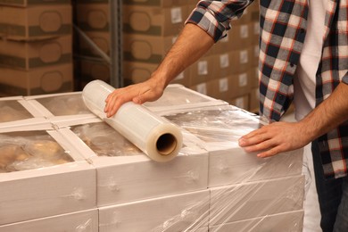 Worker wrapping boxes in stretch film at warehouse, closeup