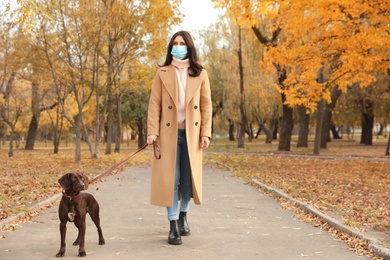 Woman in protective mask with German Shorthaired Pointer in park. Walking dog during COVID-19 pandemic