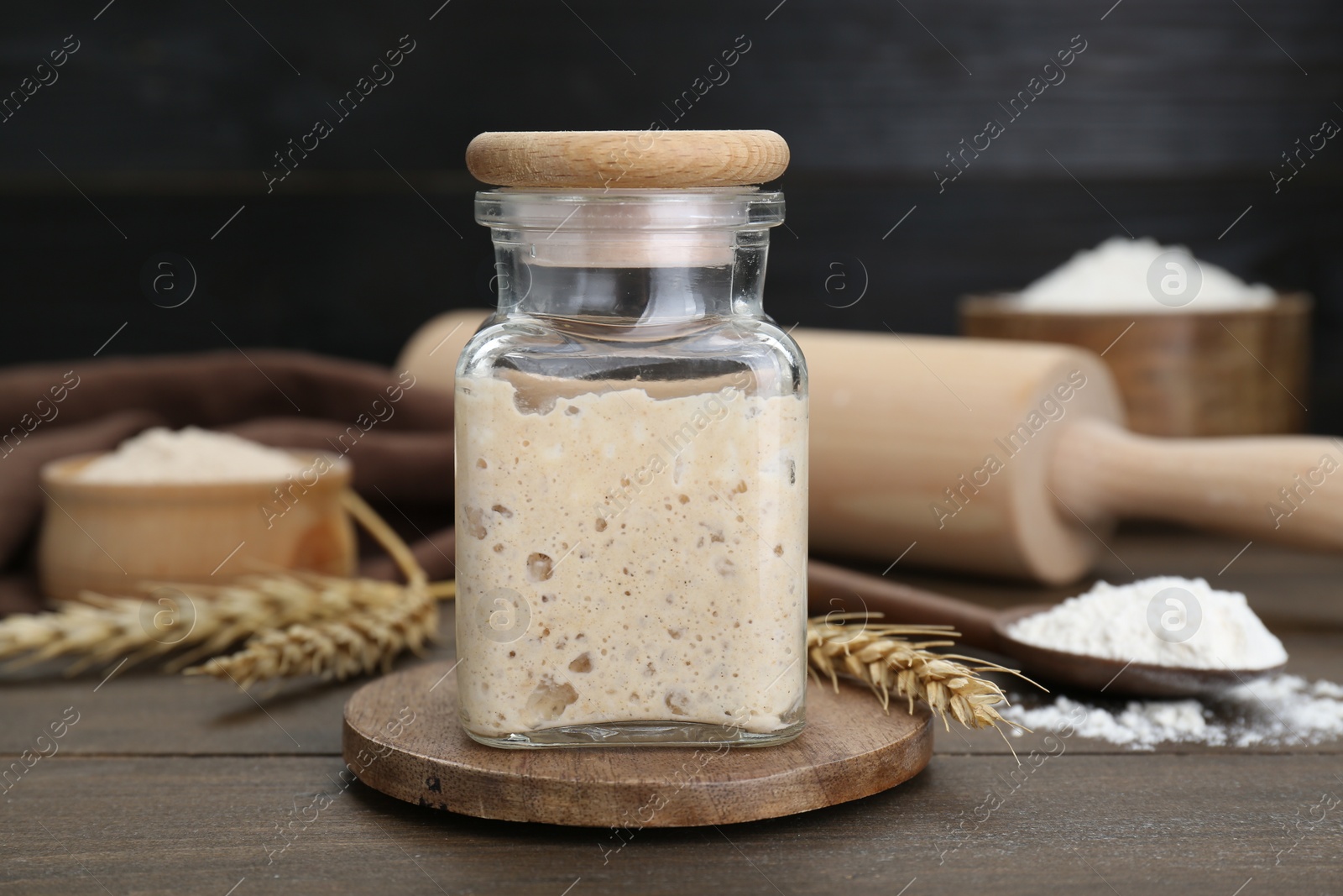 Photo of Leaven, flour and ears of wheat on wooden table