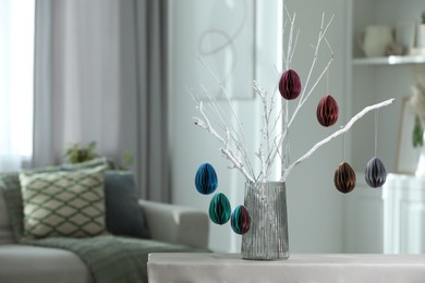 Photo of Branches with paper eggs in vase on table at home, space for text. Beautiful Easter decor.