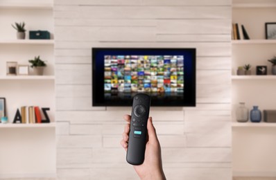 Image of Woman with remote control changing channels while watching TV at home, closeup