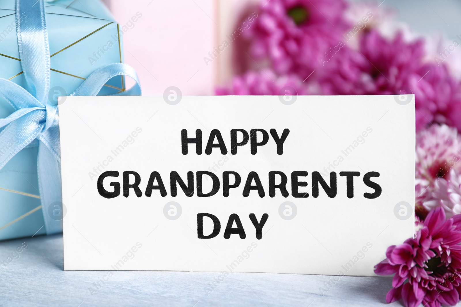 Photo of Beautiful flowers, gift boxes and card with phrase Happy Grandparents Day on grey table, closeup