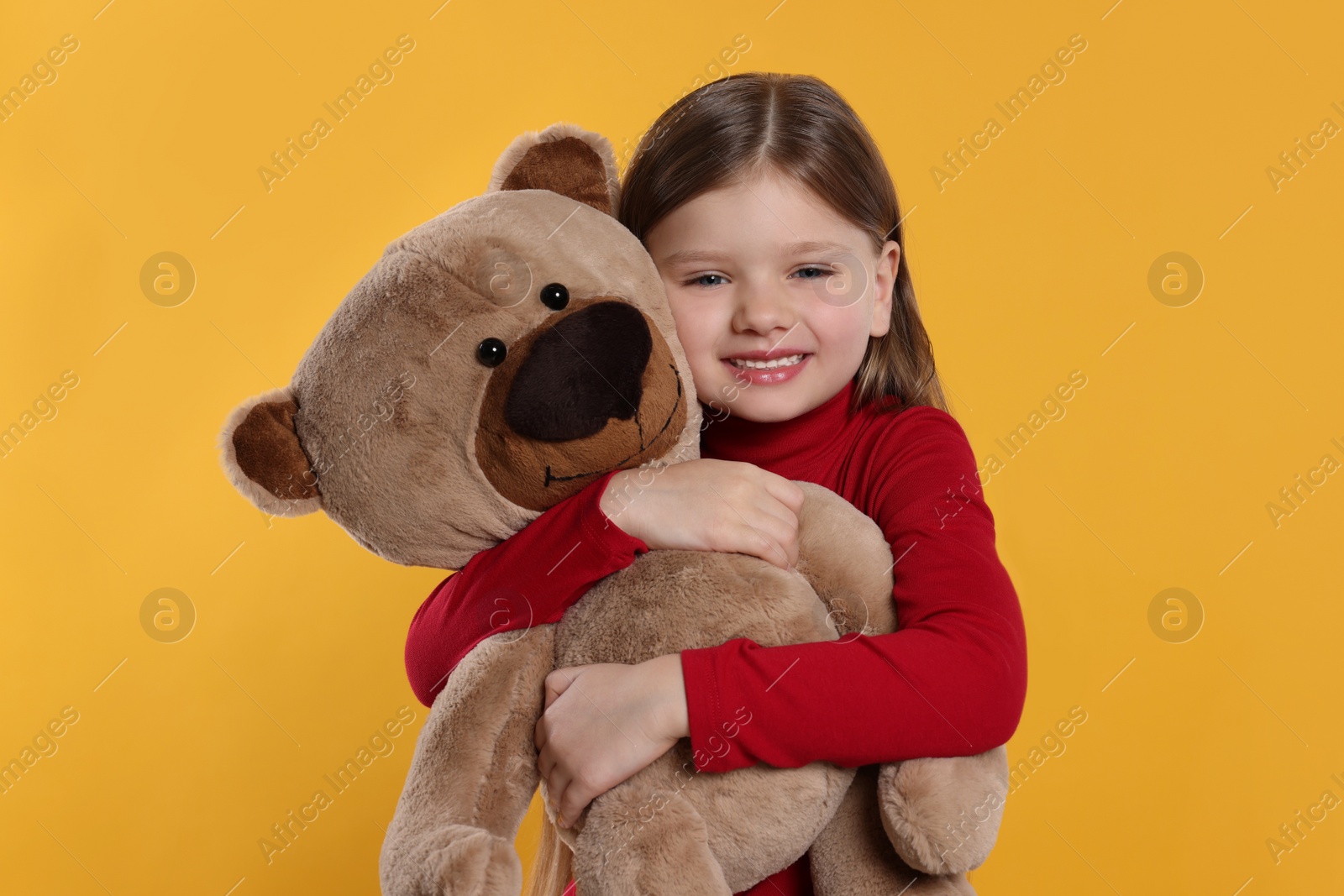 Photo of Cute little girl with teddy bear on yellow background