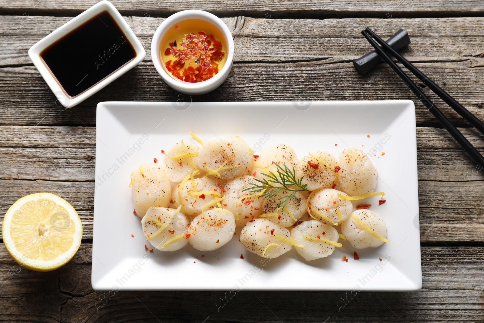 Photo of Raw scallops with spices, dill, lemon zest and sauces on wooden table, flat lay