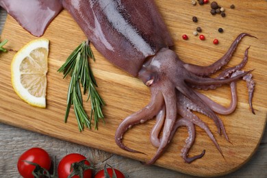 Photo of Fresh raw squid with lemon, rosemary and tomatoes on wooden table, flat lay