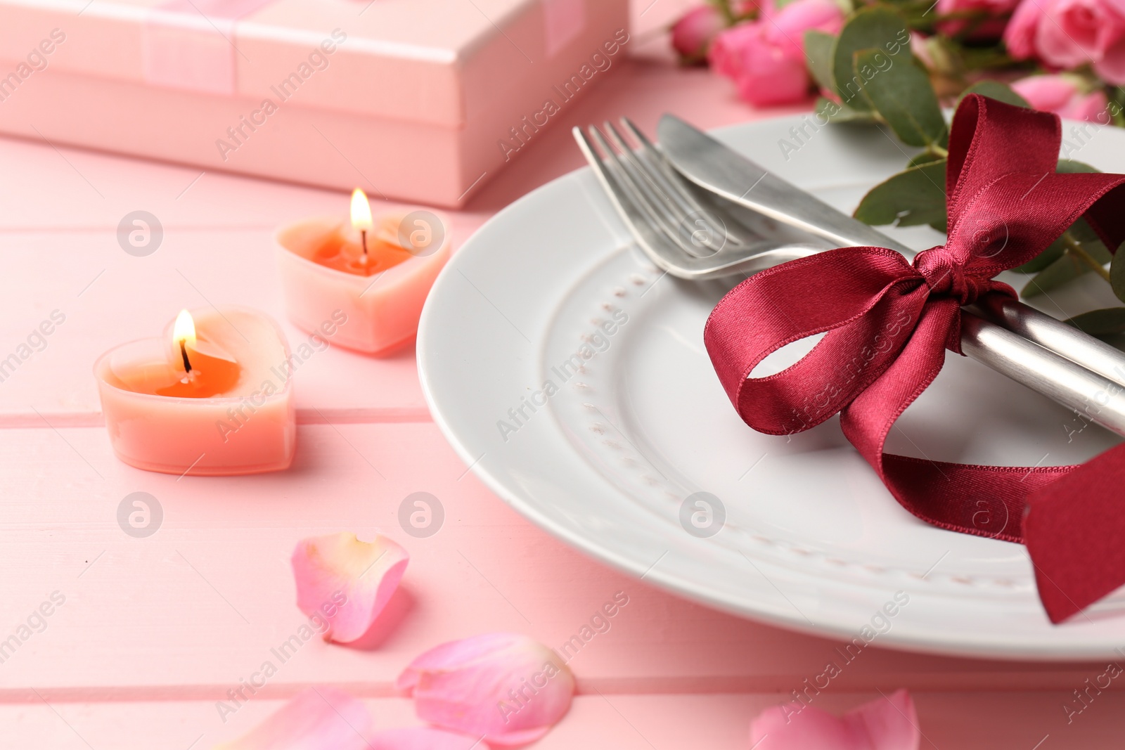 Photo of Place setting with roses and candles on pink table, closeup. Romantic dinner