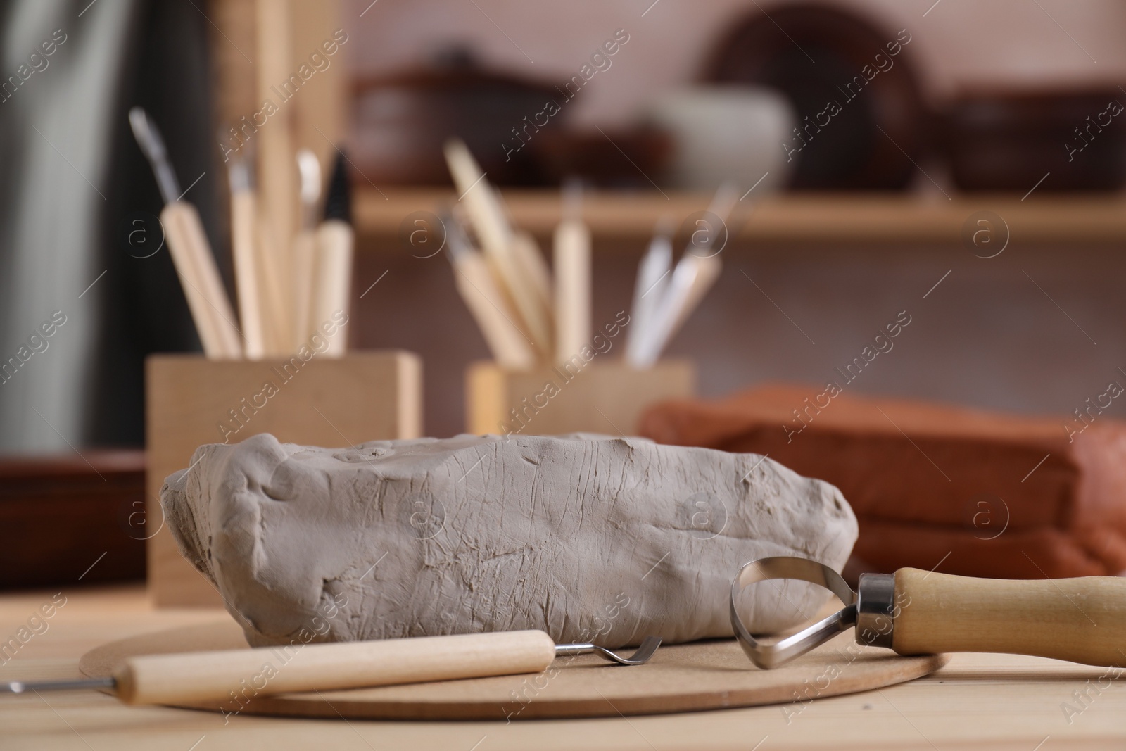 Photo of Clay and set of modeling tools on wooden table in workshop