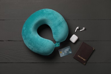 Photo of Turquoise travel pillow, passport, credit card and earphones on black wooden background, flat lay