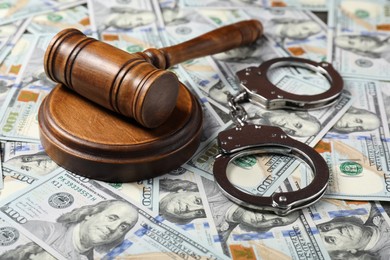 Photo of Judge's gavel and handcuffs on dollar banknotes, closeup