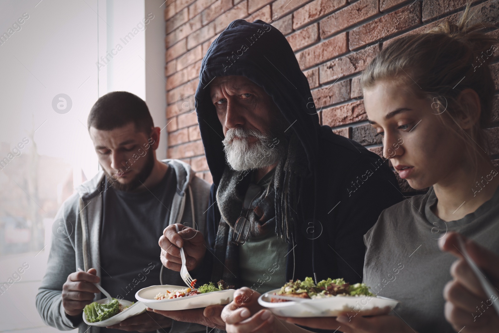 Image of Poor people with plates of food at wall indoors