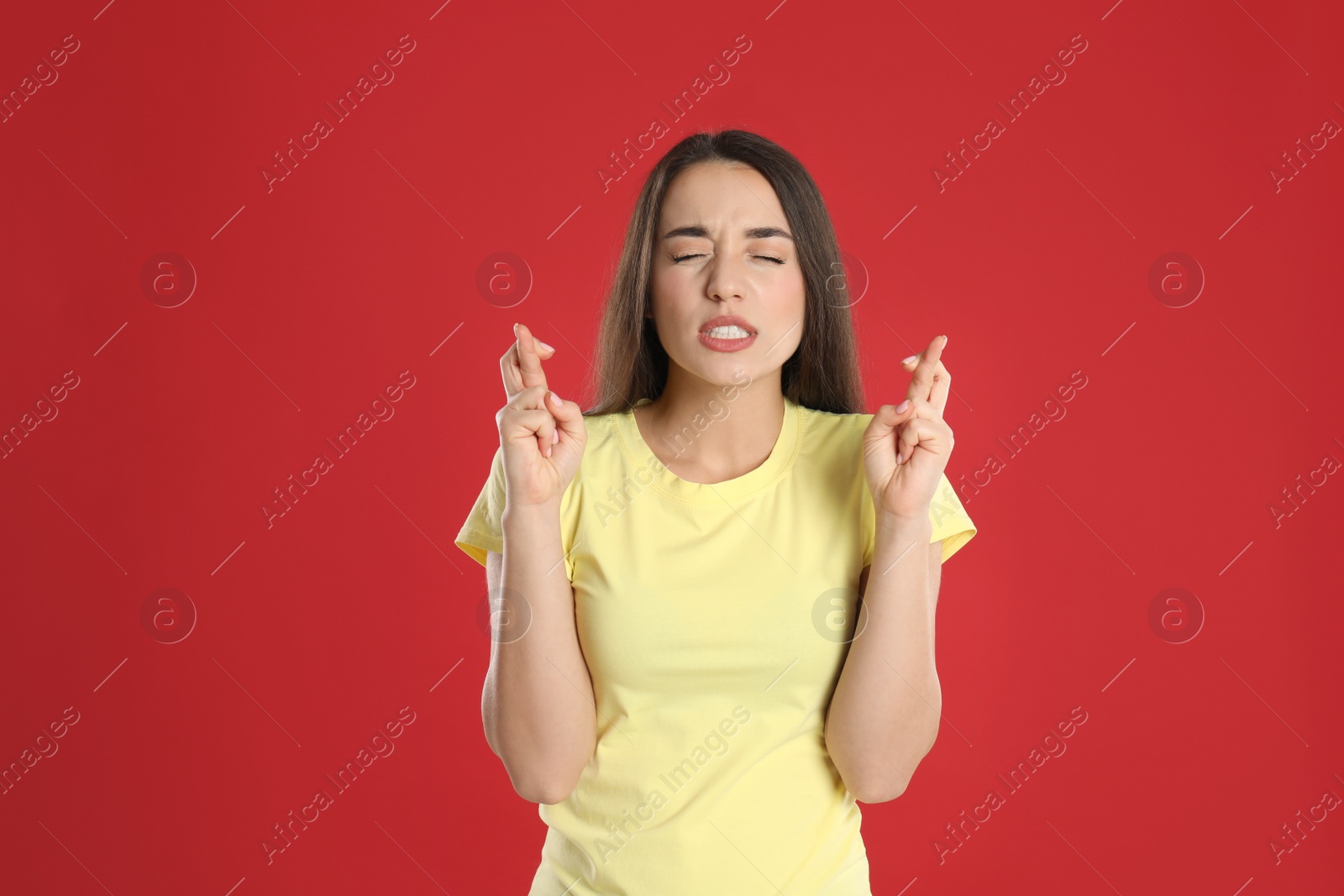 Photo of Nervous young woman holding fingers crossed on red background. Superstition for good luck 