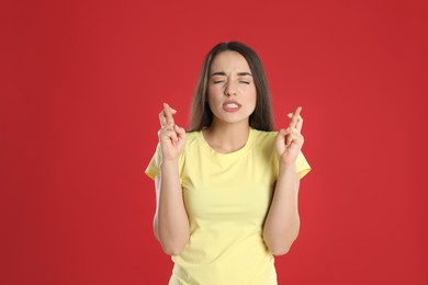 Photo of Nervous young woman holding fingers crossed on red background. Superstition for good luck 