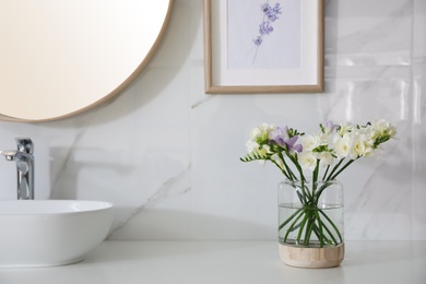 Photo of Beautiful freesia flowers on countertop in bathroom