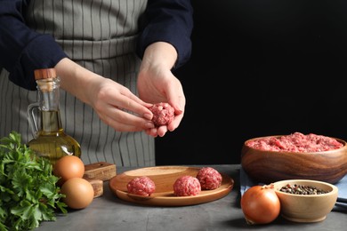 Photo of Woman making meatball from ground meat at grey table, closeup