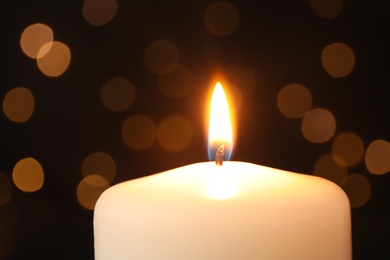 Photo of Burning candle on black background with blurred lights