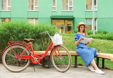 Young pretty woman reading on bench near bicycle in park