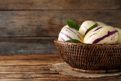 Fresh ripe pepino melons with green leaves in wicker basket on wooden table, space for text