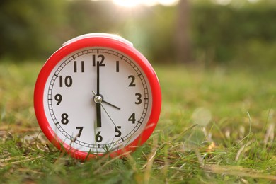 Photo of Red alarm clock on green grass outdoors. Space for text