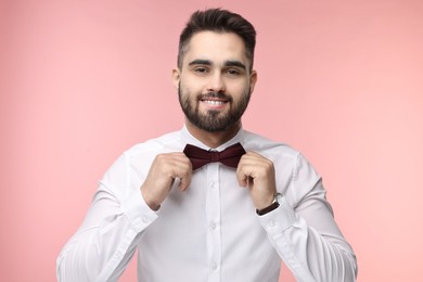 Photo of Portrait of smiling man adjusting bow tie on pink background