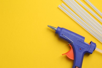 Photo of Blue glue gun and sticks on yellow background, flat lay. Space for text