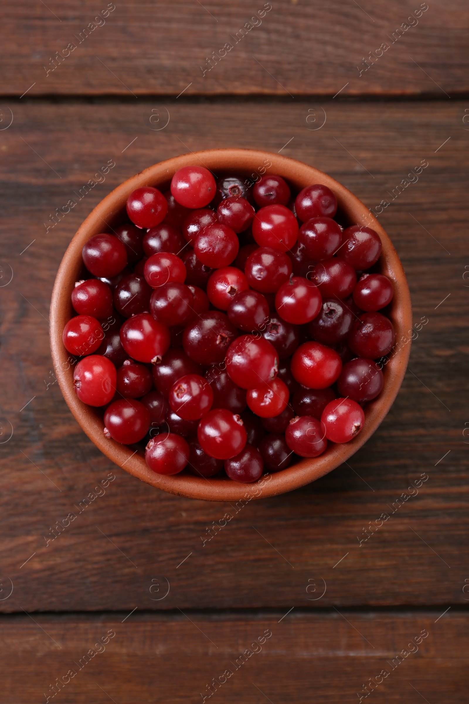 Photo of Fresh ripe cranberries in bowl on wooden table, top view