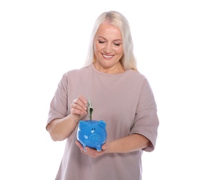 Mature woman putting money into piggy bank on white background