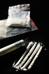 Drug addiction. Plastic bags with cocaine and rolled dollar banknote on black table, closeup