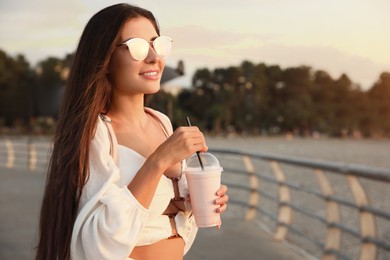 Photo of Beautiful young woman with tasty milk shake outdoors, space for text