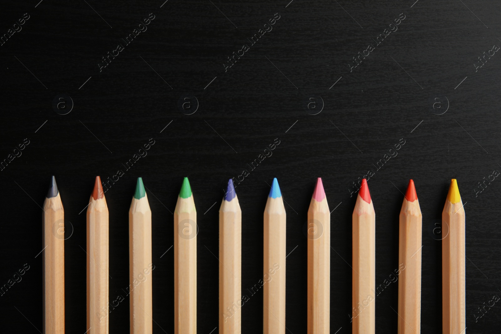Photo of Pencils of different colors with space for design on wooden background, top view. School stationery