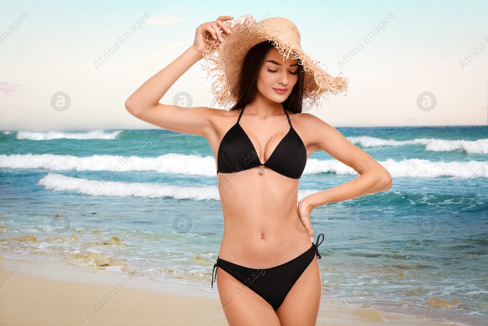 Image of Beautiful woman in stylish black bikini and hat on sandy beach near sea