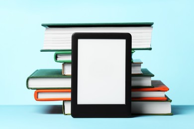Photo of Modern e-book reader and stack of hard cover books on light blue background