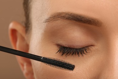 Photo of Woman applying mascara onto eyelashes against light brown background, closeup