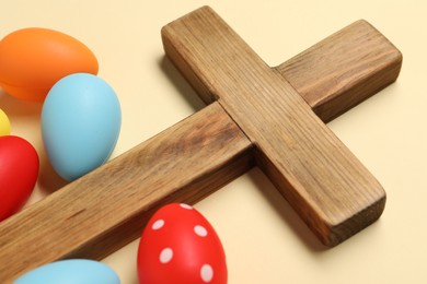 Photo of Wooden cross and painted Easter eggs on beige background, closeup