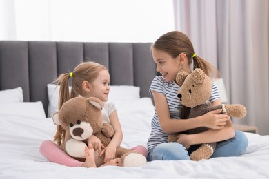 Photo of Cute little sisters with teddy bears on bed at home